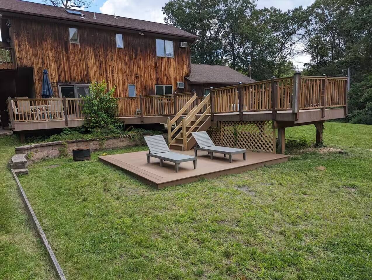 Eine Holzterrasse mit zwei Liegestühlen, einer Treppe und einem Holzzaun.