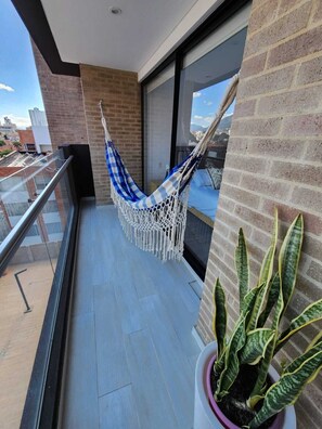A balcony with a hammock, a potted plant, and a view of the cityscape. - Cozy and sophisticated apartment with a pool, gym, and spa in the Financial District (Bogotá)