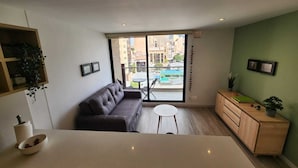 A modern living room with a sofa, a small round table, a wooden cabinet, and a view through a glass door to the outside. - Cozy and sophisticated apartment with a pool, gym, and spa in the Financial District (Bogotá)