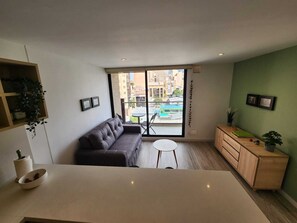A modern living room with a sofa, a small round table, a wooden cabinet, and a view through a glass door to the outside. - Cozy and sophisticated apartment with a pool, gym, and spa in the Financial District (Bogotá)