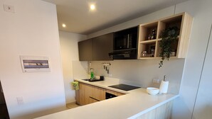 A modern kitchen with a white countertop, two black bar stools, a black microwave, and wooden cabinets. - Cozy and sophisticated apartment with a pool, gym, and spa in the Financial District (Bogotá)