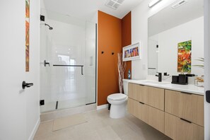 A modern bathroom with a glass shower enclosure, a white toilet, and a wooden vanity with a large mirror.
