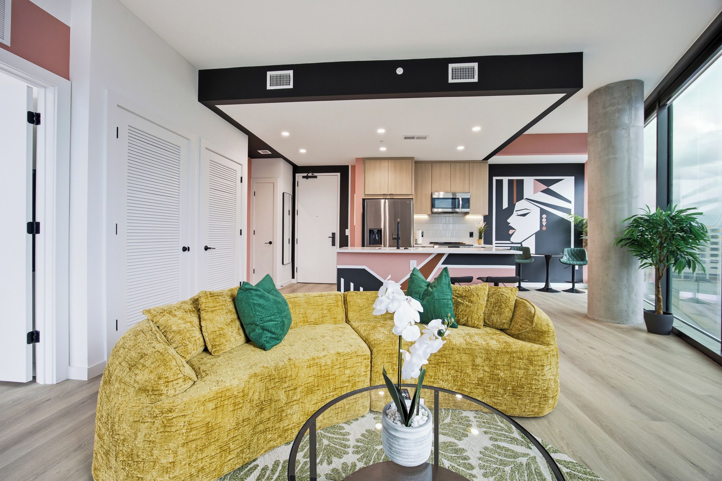Ein modernes Wohnzimmer mit einem gelben Sofa, einem Couchtisch mit Pflanze und Blick auf die Küche und den Essbereich.