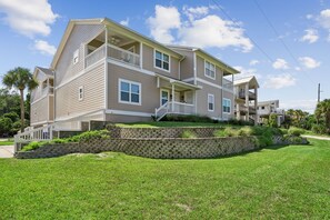 A multi-story residential building with a porch, stone retaining wall, and a well-maintained lawn. - 3BR/3BA Multilevel Condo | Steps to Pool & Beach | Monthly Stays (Fernandina Beach)