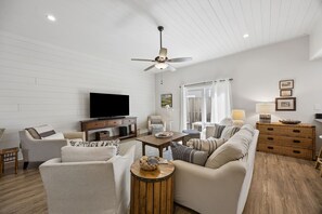 A living room with a television, sofa, armchair, coffee table, and a ceiling fan. - 3BR/3BA Multilevel Condo | Steps to Pool & Beach | Monthly Stays (Fernandina Beach)