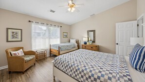 Ein Schlafzimmer mit einem Bett, zwei Nachttischen, einem Sessel, einem Deckenventilator und einem Fenster mit Jalousien.