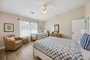 A bedroom with a bed, two bedside tables, a chair, a ceiling fan, and a window with blinds. - 3BR/3BA Multilevel Condo | Steps to Pool & Beach | Monthly Stays (Fernandina Beach)