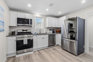 A modern kitchen with stainless steel appliances, white cabinetry, and a window providing natural light. - North End 5BR/ 2.5BA Unit 2 - Walk to Beach & Boardwalk (Ocean City)