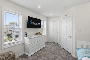 Un dormitorio con un ventanal amplio, un televisor de pantalla plana montado en la pared, un aparador blanco y una puerta.