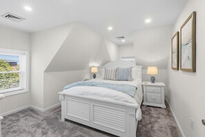 A bedroom with a sloped ceiling, a bed with white bedding, two bedside tables with lamps, and a window with blinds. - North End 5BR/ 2.5BA Unit 2 - Walk to Beach & Boardwalk (Ocean City)