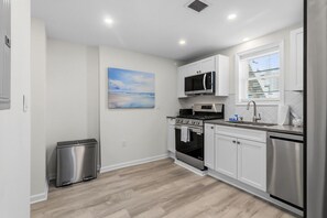 Una cocina moderna con armarios blancos, electrodomésticos de acero inoxidable y vistas al exterior a través de un ventanal.