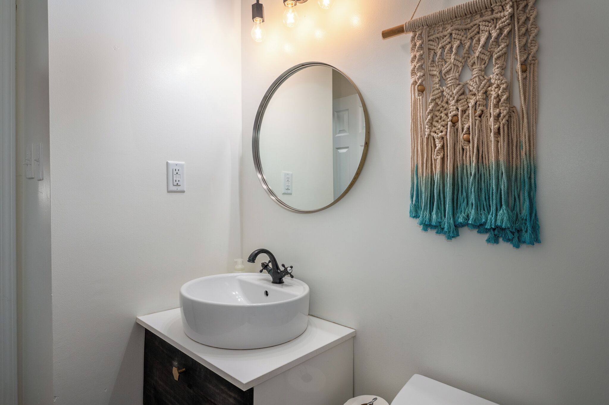 A bathroom with a white sink, a round mirror, and a macrame towel.