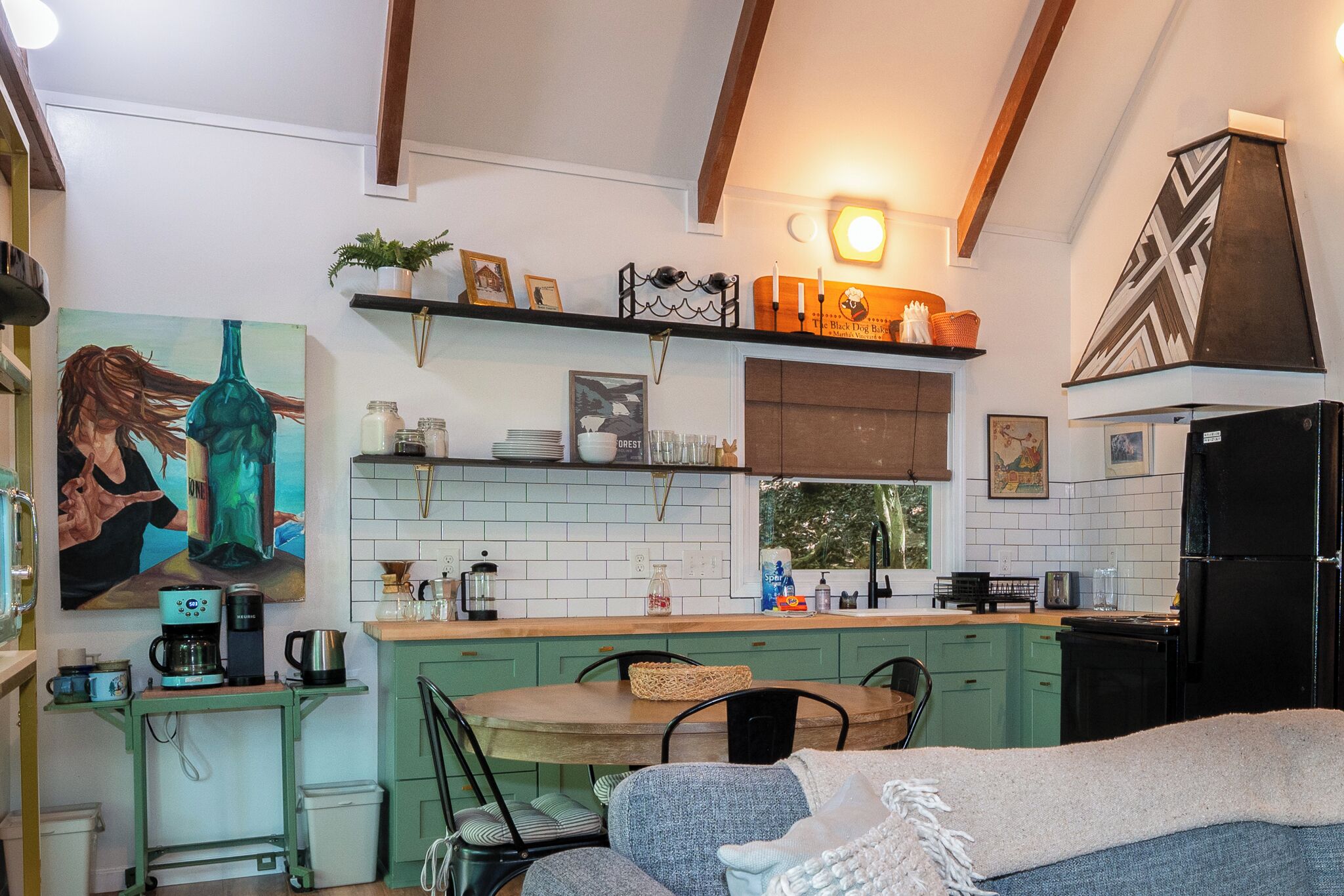 A cozy kitchen with a dining area, featuring a coffee maker, a kettle, and a painting on the wall.