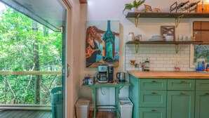 Una cocina con cafetera, un lavamanos y una ventana con vistas a la vegetación.