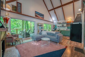 Ein geräumiger Wohnbereich mit großem Sofa, Couchtisch und Esstisch. Eine Küchenzeile mit Kühlschrank und Mikrowelle ist ebenfalls vorhanden. Das Zimmer verfügt über große Fenster und Blick ins Freie.