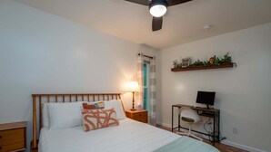 Un dormitorio con cama, mesita de noche, lámpara y escritorio con computadora.