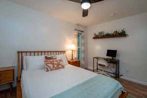 Ein Schlafzimmer mit Bett, Nachttisch, Lampe und Schreibtisch mit Computer.