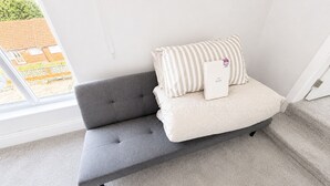 En grå soffa med randiga kuddar och en etikett, placerad framför en vit vägg med ett fönster.