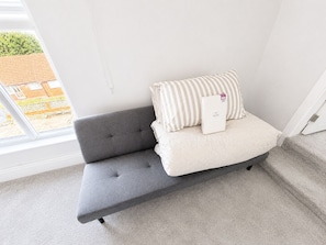 Ein graues Sofa mit gestreiften Kissen und einem Etikett, vor einer weißen Wand mit einem Fenster platziert.
