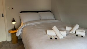 En snyggt bäddad säng med vita lakan och handdukar, en sänglampa och ett litet träbord bredvid sängen.