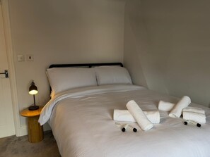 Ein ordentlich bezogenes Bett mit weißen Leinen und Handtüchern, eine Nachttischlampe und ein kleiner Holfnachtisch.