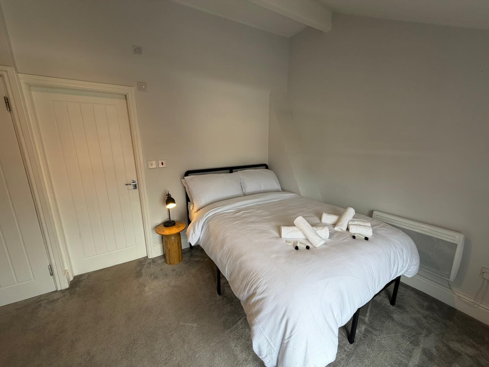 Une chambre à coucher avec un lit, une table de chevet avec une lampe et une porte.