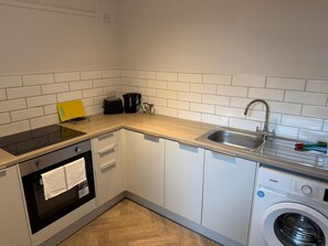 Una cucina compatta con forno a incasso, macchina da caffè, lavello e lavatrice.