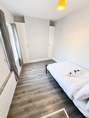 Ein Schlafzimmer mit einem Bett, einem Heizkörper, einem Kleiderschrank und einem Fenster mit Vorhängen.
