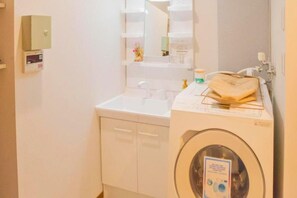 A compact bathroom with a washing machine, a sink, and a mirror.