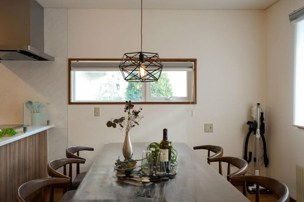 A dining area with a long table, chairs, a hanging light fixture, and a window with a view.