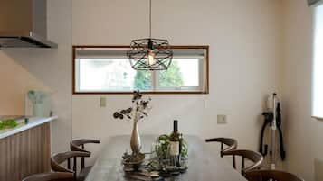 A dining area with a long table, chairs, a hanging light fixture, and a window with a view.