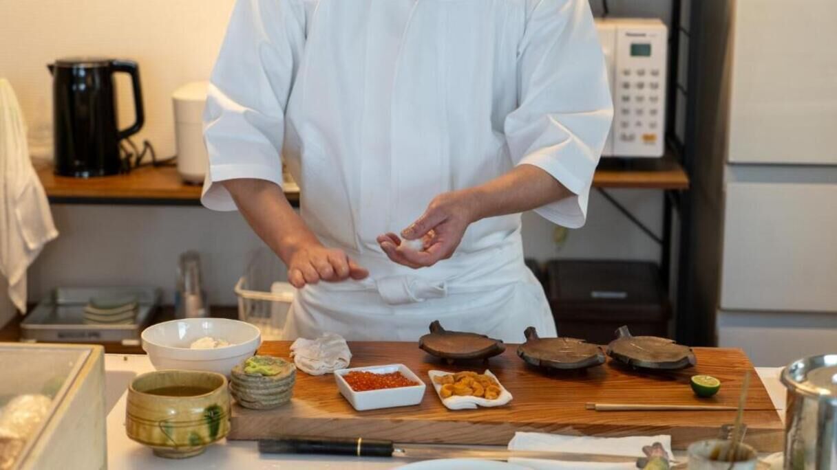 A chef preparing food in a kitchen with various ingredients and utensils on the counter.