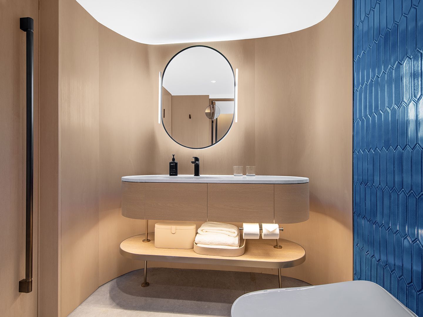 Un baño moderno con un espejo redondo, un lavamanos con toallero y un inodoro.