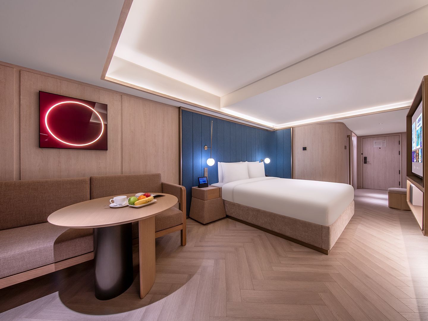 A modern hotel room with a bed, a sofa, a small table with breakfast, and a wall-mounted TV.