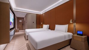 Ein Hotelzimmer mit zwei Betten, einem Nachttisch mit Lampe und einem digitalen Bildschirm.