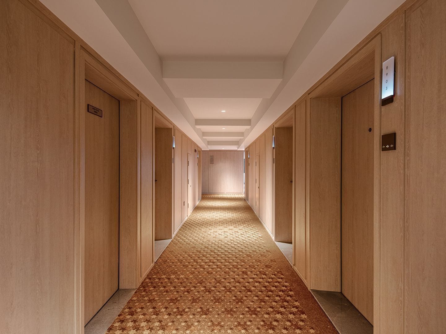 Un pasillo de hotel con puertas de madera, un suelo estampado y un techo con iluminación empotrada.
