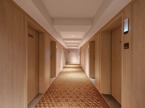 Un pasillo de hotel con puertas de madera, un suelo estampado y un techo con iluminación empotrada.