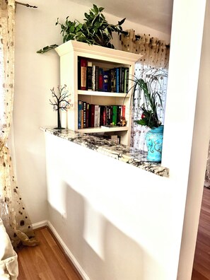 Una estanteria amb llibres i objectes decoratius, una planta petita en forma d'arbre i un vas blau amb una planta.