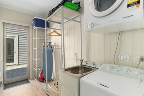 A laundry room with a washing machine, a sink, and a drying rack.