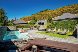 A pool area with stone walls, lounge chairs, and a wooden deck.
