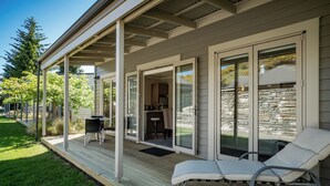 A covered outdoor area with a patio, a dining table, chairs, and a lounge chair. - Cardrona Haven - Resort spa & swimming pool! (Cardrona)