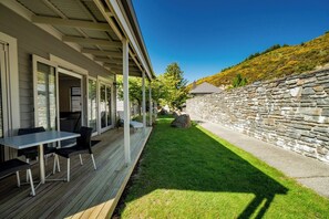 A covered outdoor area with a table and chairs, a stone wall, and a grassy lawn.