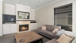 A living room with a fireplace, a sofa, a television, and a window with blinds. - Cardrona Haven - Resort spa & swimming pool! (Cardrona)