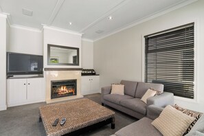 Ein Wohnzimmer mit Kamin, einer Couch, einem Fernseher und einem Fenster mit Jalousien.
