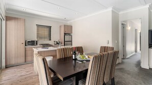 A modern kitchen with a dining area, featuring a wooden table and striped chairs, a microwave, and a refrigerator. - Cardrona Haven - Resort spa & swimming pool! (Cardrona)
