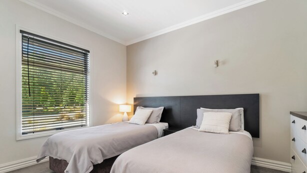 A bedroom with two beds, a nightstand, a lamp, and a window with blinds. - Cardrona Haven - Resort spa & swimming pool! (Cardrona)