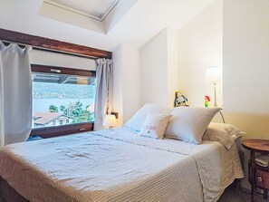 Een hotelkamer met een bed, een raam met gordijnen, een nachtkastje en een lamp.