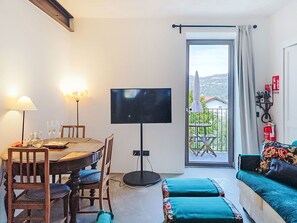 Ein Zimmer mit Esstisch, Stühlen, Fernseher, Sofa und einem Balkon mit Blick.