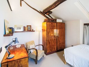 Ein Schlafzimmer mit einem Bett, einem Schreibtisch mit Lampe, einem Sessel, einem Kleiderschrank und einem Regal mit gerahmten Bildern.