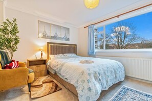 A bedroom with a bed, a nightstand, a lamp, a chair, a window with a view, and a plant. - #99 Quirky and Stylish 3-Bed Tamworth Centre Home (Staffordshire)